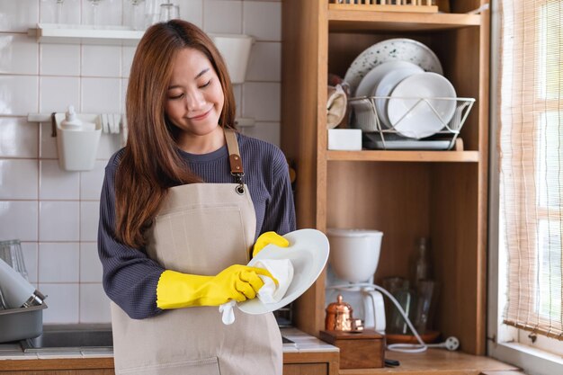 Uma dona de casa usando avental e luva protetora limpando e lavando pratos na cozinha em casa