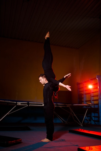 Uma dupla de acrobatas executando uma manobra de duplas. Uma mulher de macacão de ginástica e um homem de roupa esportiva. Artistas de circo muito flexíveis.