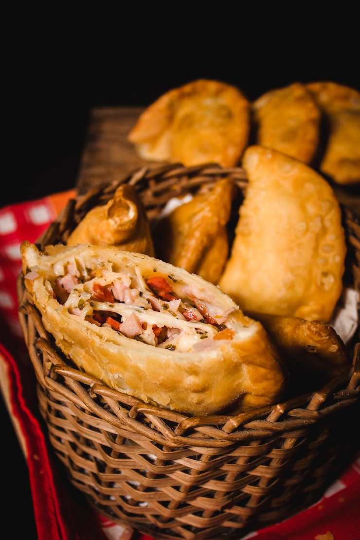 Foto uma empanada napolitana aberta ao meio, com um conjunto de empanadas em cima de uma toalha de mesa vermelha