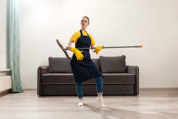 Uma empregada de casa alegre, de avental e luvas, limpa as casas e dança com um esfregão.