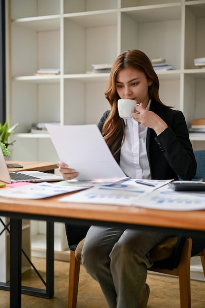 Uma empresária analisando relatórios financeiros de negócios enquanto toma café em sua mesa