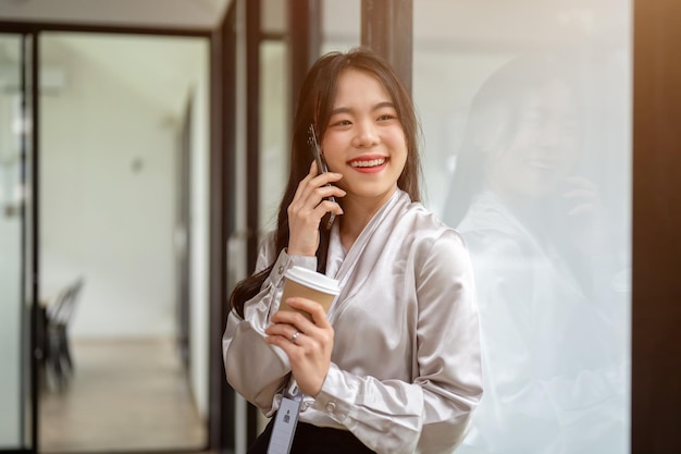 uma empresária asiática atraente está falando ao telefone enquanto está em um corredor de escritório