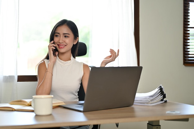 Uma empresária asiática bem-sucedida e confiante está ao telefone com seu fornecedor de negócios