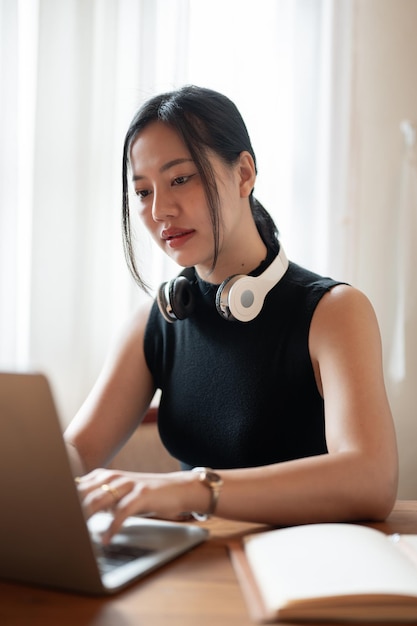 Uma empresária asiática focada e profissional trabalhando em seu laptop em uma mesa dentro de casa