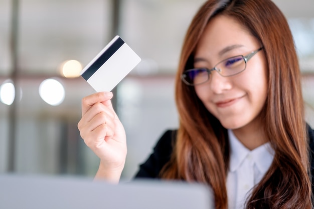 Uma empresária asiática segurando um cartão de crédito enquanto usa um laptop no escritório