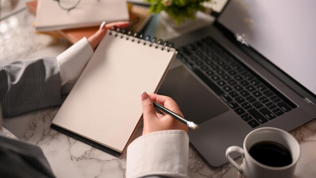 Uma empresária elegante tomando notas em seu bloco de notas em espiral sobre sua mesa de escritório moderna fechada