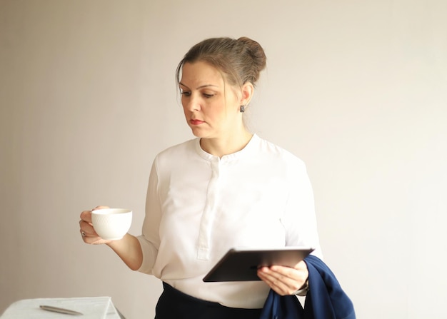Uma empresária em roupas de escritório com café e um tablet nas mãos está estudando documentos