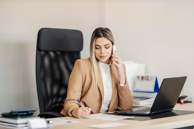 Uma empresária está sentada em seu local de trabalho conversando com o cliente e cuidando da papelada Conceito de multitarefa