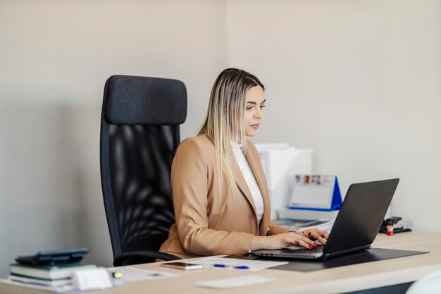 Uma empresária focada está sentada em seu escritório e terminando o relatório no laptop