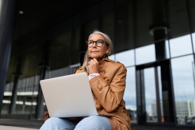 Uma empresária senta-se com um laptop de joelhos nos degraus da entrada de um prédio de escritórios
