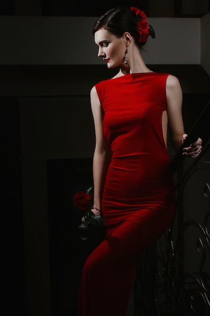 Foto uma encantadora jovem sensual em um vestido de elegância e rosa vermelha na mão está andando no evento.