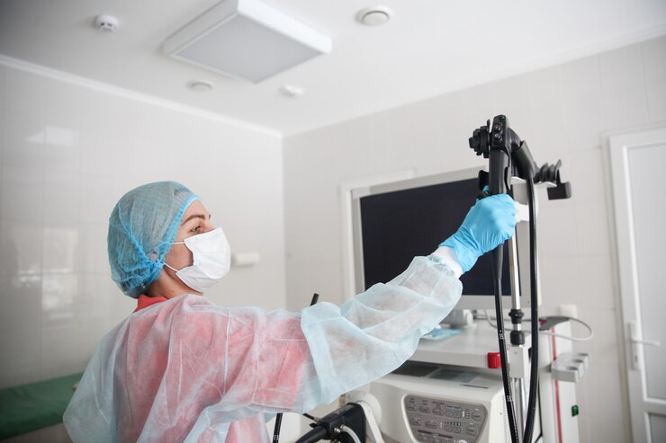 Uma endoscopista cirurgiã com traje de proteção, boné, máscara e luvas pega um endoscópio antes de iniciar o procedimento
