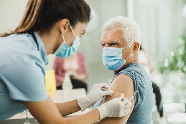 Uma enfermeira aplicando um band-aid a um idoso depois de receber uma vacina devido à epidemia de coronavírus.