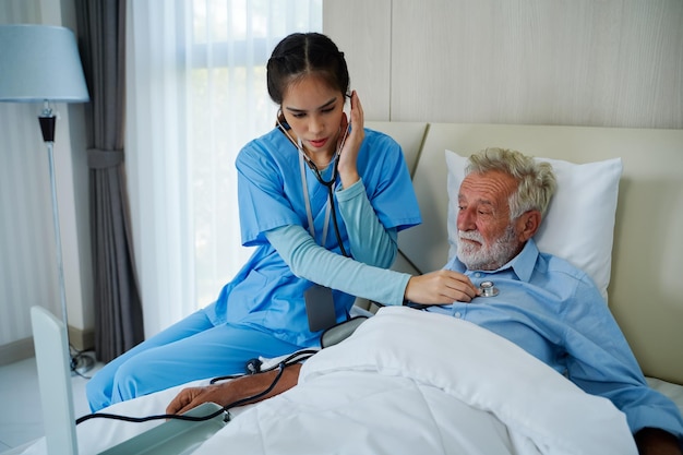 Uma enfermeira com um estetoscópio ouve um paciente idoso Verifique o coração verifique os idosos se aposentam em casa Doença cardíaca idosa Conceito de doença cardíaca