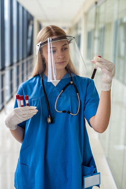 Uma enfermeira de uniforme com tampa protetora segura tubos de ensaio com amostras de sangue