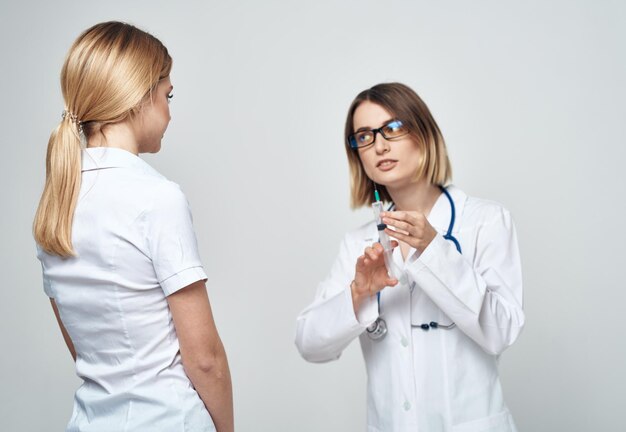 Uma enfermeira segura uma seringa na mão sobre um fundo claro com um estetoscópio e uma paciente do sexo feminino