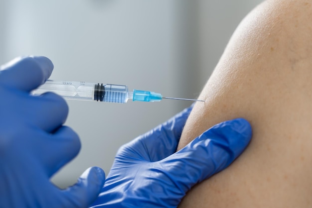 Uma enfermeira vacina um paciente em close-up do ombro. Vacinação obrigatória durante uma perigosa epidemia de gripe.