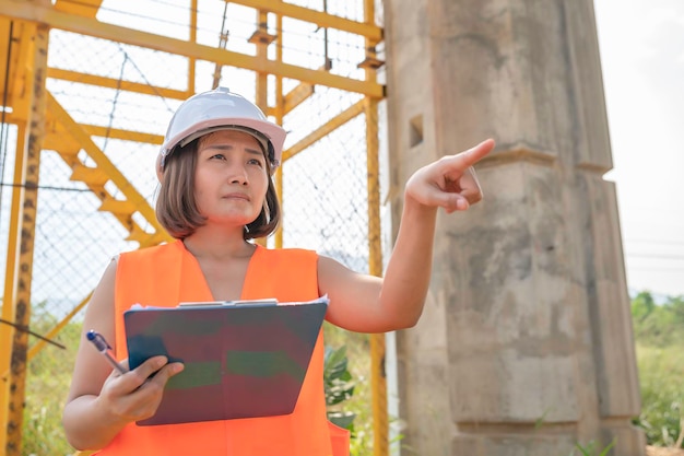 Uma engenheira asiática trabalha em um canteiro de obras de ponte de autoestradaTrabalhador civil inspecionando o trabalho na construção de travessia