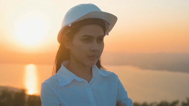 Uma engenheira está colocando um capacete protetor na cabeça ao pôr do sol.