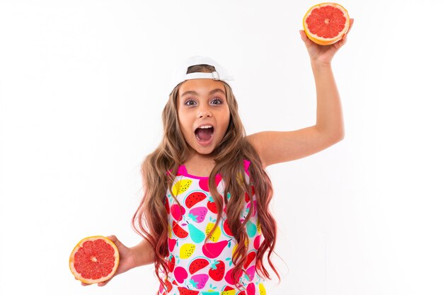 Uma engraçadinha caucasiana com cabelos longos, maiô, boné branco detém metades de toranja e sorrisos