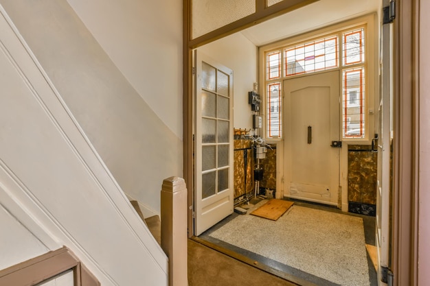 Uma entrada em uma casa com paredes brancas e guarnição de madeira nas janelas da porta e piso acarpetado