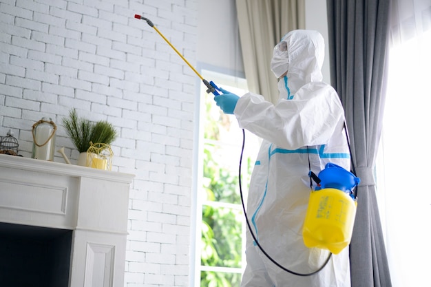 Uma equipe médica em traje de EPI está usando spray desinfetante na sala de estar, proteção Covid-19, conceito de desinfecção.