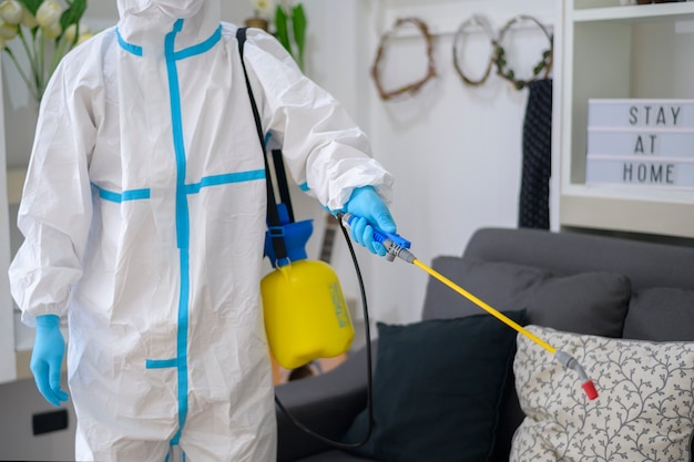 Uma equipe médica em traje de epi está usando spray desinfetante na sala de estar, proteção covid-19, conceito de desinfecção.