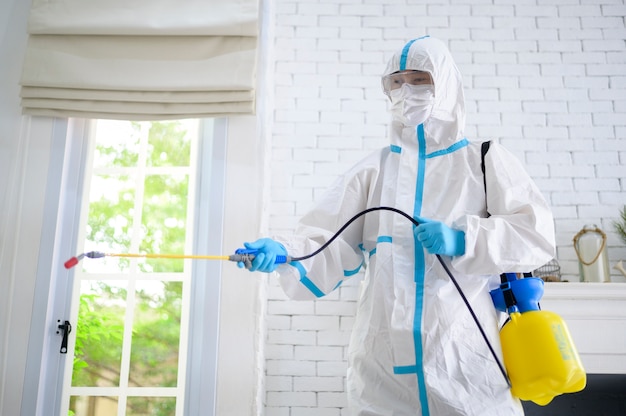 Uma equipe médica em traje de EPI está usando spray desinfetante na sala de estar, proteção Covid-19, conceito de desinfecção.