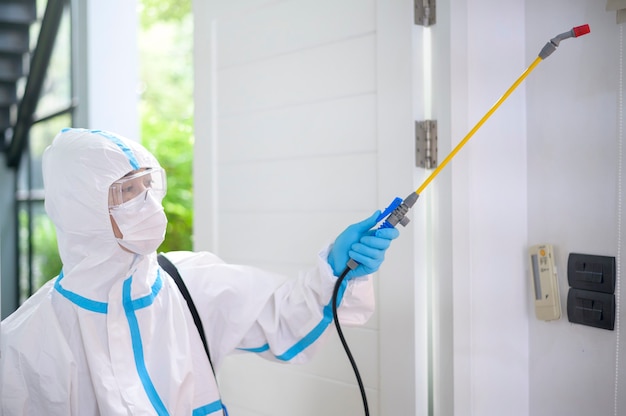 Uma equipe médica em traje de EPI está usando spray desinfetante na sala de estar, proteção Covid-19