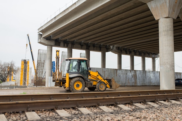 Uma escavadeira de construção passa sob uma ponte rodoviária de concreto armado em construção