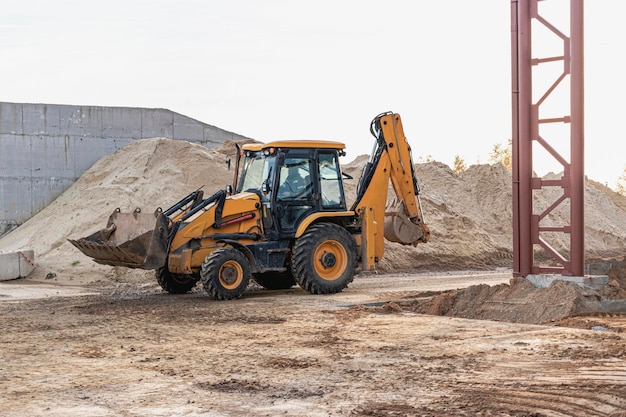 Uma escavadeira na caçamba dianteira remove o solo para aterro no canteiro de obras. Equipamento de construção para terraplenagem.