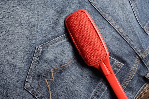 uma escova de plástico vermelho para limpar roupas encontra-se em jeans preto.