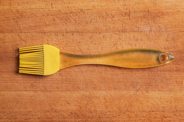 Foto uma escova de silicone de cozinha amarela senta-se em uma placa de corte desgastada