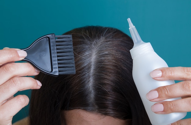 Uma escova e uma garrafa em mãos femininas sobre cabelos grisalhos. Conceito de cor de cabelo grisalho