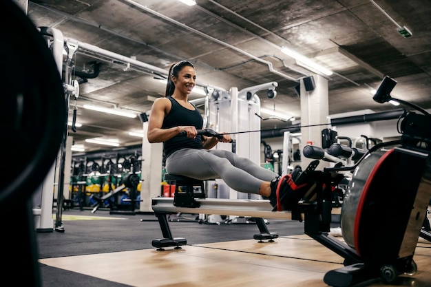 Uma esportista forte e saudável está fazendo exercícios em uma máquina de remo em uma academia