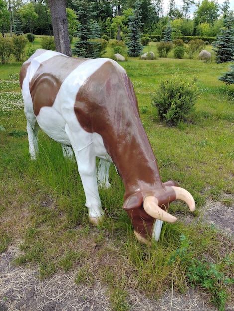 Uma estátua de uma vaca no parque como decoração em tamanho real sobre um fundo de grama e árvores