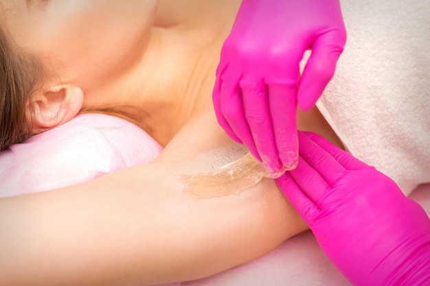 Uma esteticista aplica uma depilação em pasta de açúcar sob a axila feminina em um salão de beleza, de perto.