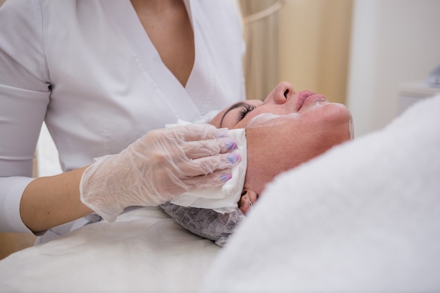 Foto uma esteticista de uniforme branco e boné limpa o rosto da cliente