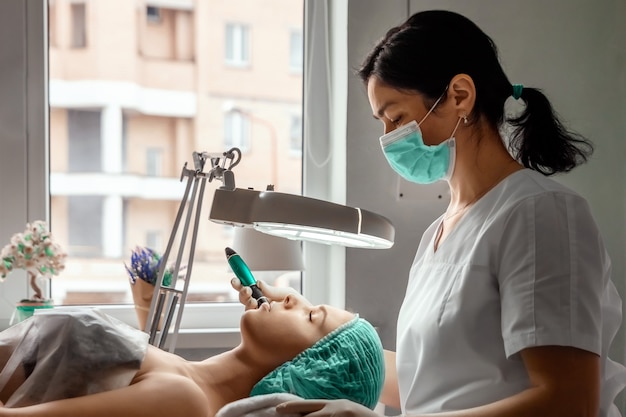 Uma esteticista usando luvas médicas limpa os poros do rosto usando um equipamento especial