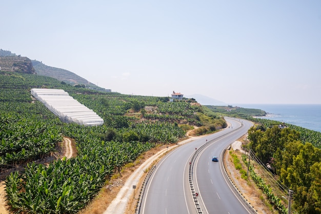 Uma estrada de asfalto vazia serpenteia ao longo da costa cênica de tirar o fôlego em um dia ensolarado de verão. Uma foto espetacular de uma estrada costeira com vista para o céu azul e o calmo Mar Mediterrâneo.