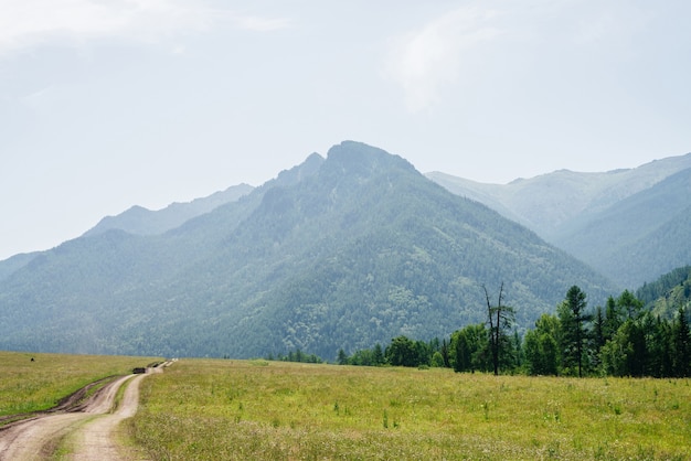 Uma estrada de terra sinuosa leva a uma montanha gigante com uma floresta de coníferas na névoa