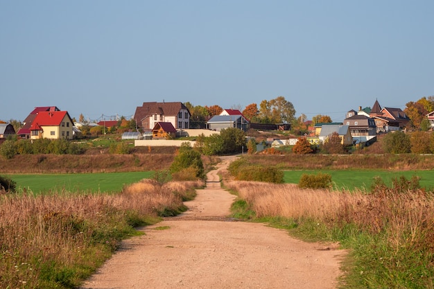 Uma estrada de terra vazia para uma colina com chalés. Rússia.