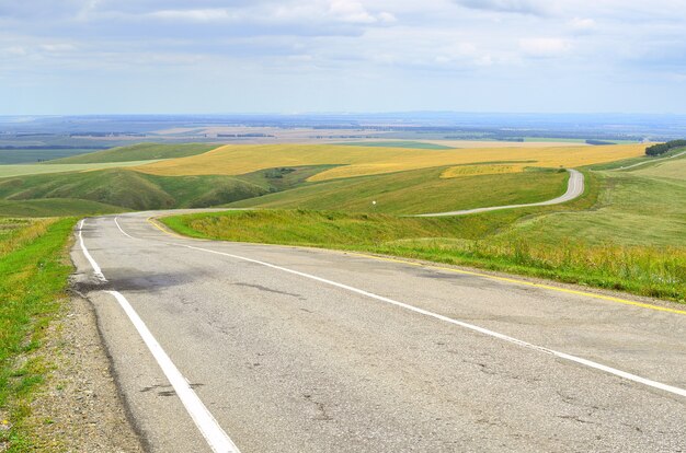 Uma estrada regional em uma área rural nas estepes no contexto de colinas verdes sob um céu nublado. sibéria, rússia