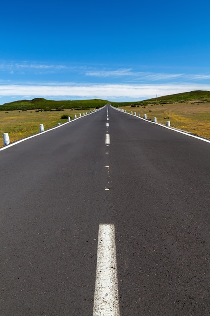 Uma estrada reta sobre a área com um céu azul e nuvens ao longe