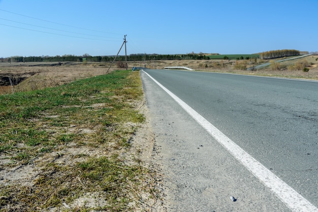 Uma estrada sinuosa que se estende ao longe, tendo como pano de fundo uma bela paisagem de primavera, campos, prados, florestas e colinas. Listras de estrada no asfalto. A perspectiva de fazer uma viagem.