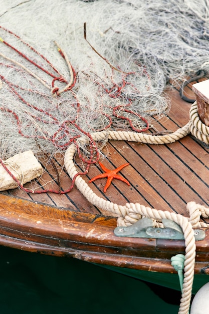 Foto uma estrela-do-mar laranja deitada no convés de um barco de madeira perto de uma corda e uma rede de pesca de perto