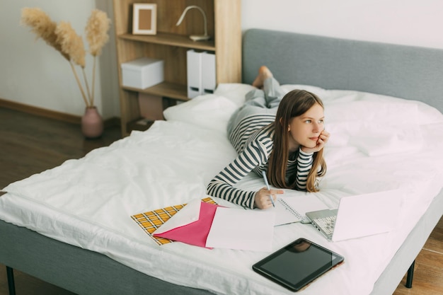 Foto uma estudante bonita e inteligente está deitada na cama em casa preparando-se para o exame com um laptop