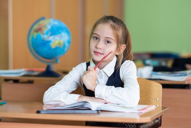 Uma estudante bonita se senta em uma mesa cercada por livros Olha para a câmera Vida escolar