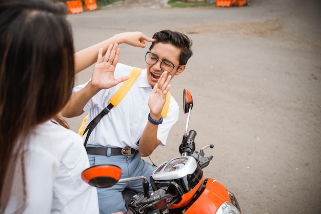 Uma estudante do ensino médio aponta para a cabeça de um estudante do sexo masculino com óculos andando de moto