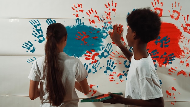 Foto uma estudante do liceu e um rapaz africano pintam a parede com as mãos.